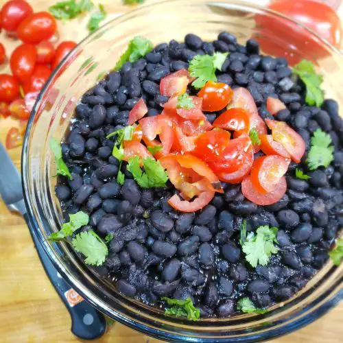 overhead image of glass bowl of cooked black beans garnished with chopped tomatoes and cilantro