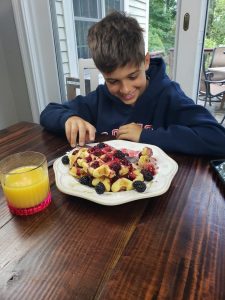 smiling boy eats waffles with blackberry sauce