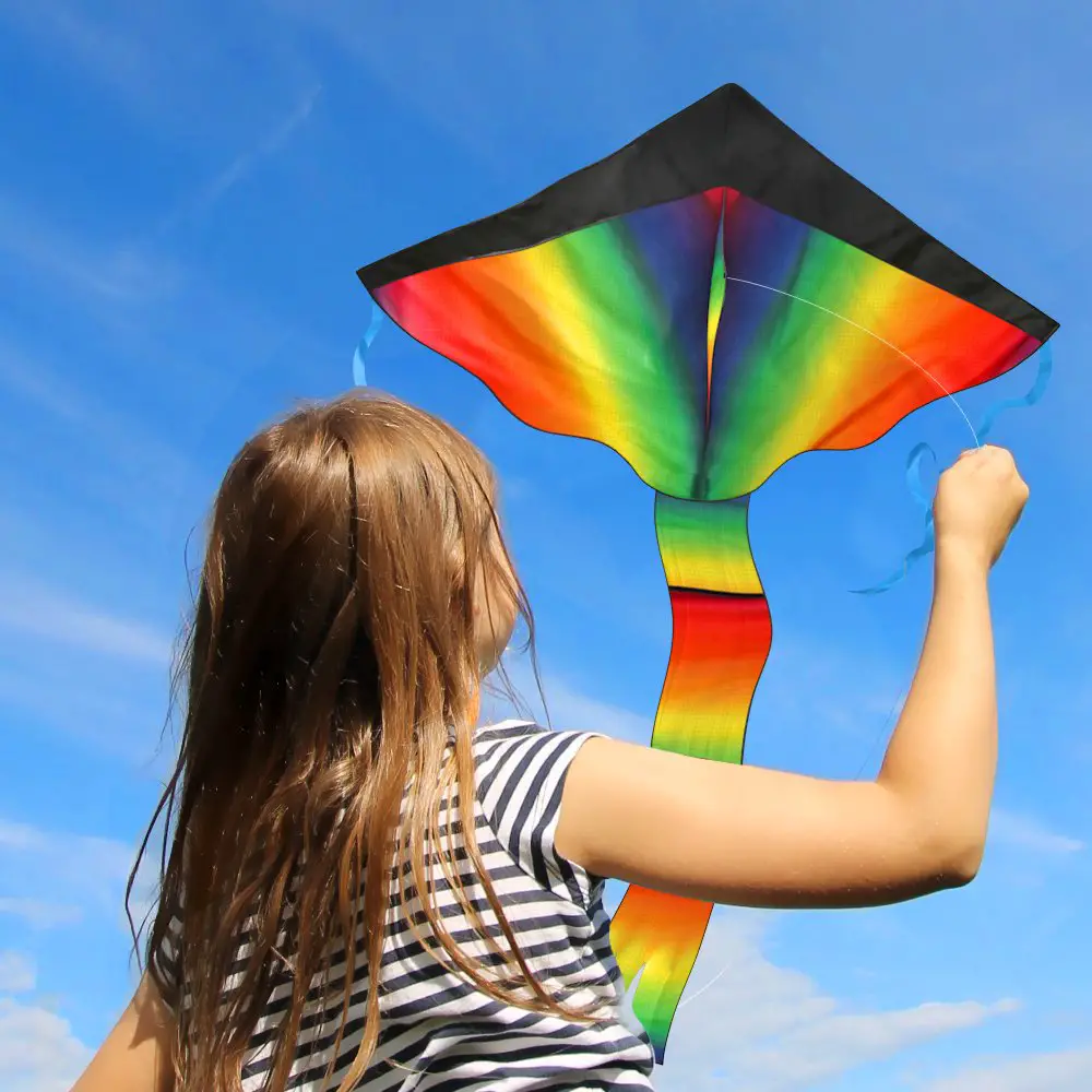 little girl flies rainbow kite in the air