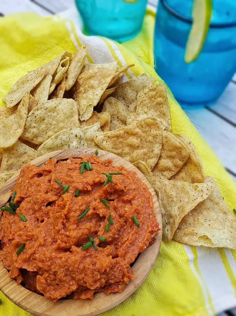 white bean chipotle dip served with tortilla chips on bright yellow linen napkin with blue tumbler glass in background