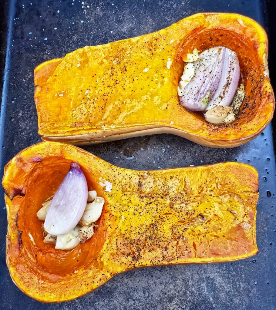 over head image of roasted butternut squash on a sheet pan with shallots and garlic cloves drizzled with olive oil and seasoned with salt and pepper