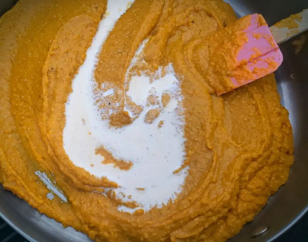 image of milk being incorporated into butternut squash puree with a pink spatula
