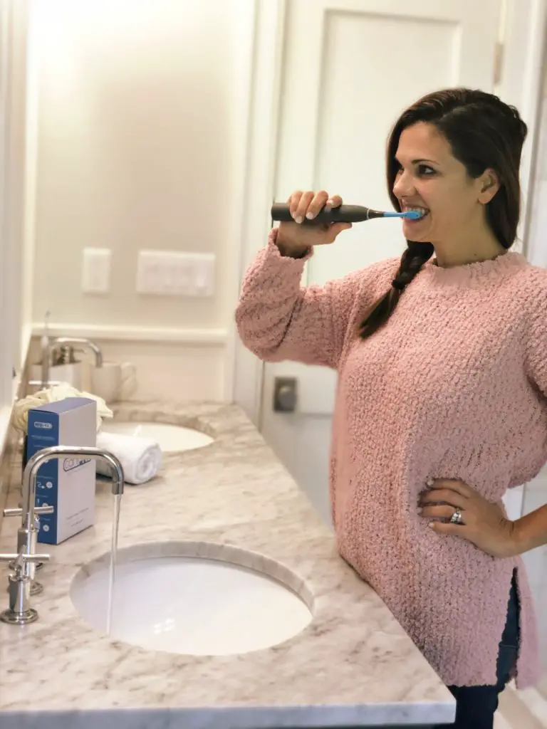 girl wearing pink sweater brushing teeth with electric toothbrush