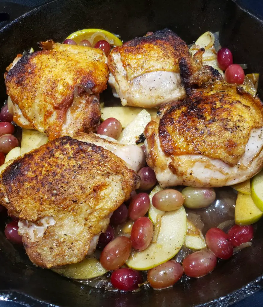 seared chicken thighs in cast iron skillet with apples and grapes