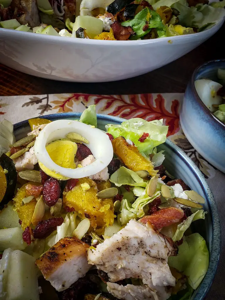 an individual serving of a harvest cobb next to a large bowl of harvest cobb salad