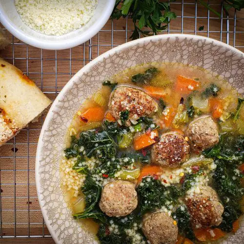 bowl of italian wedding soup with focaccia bread and grated parmesan cheese bowl
