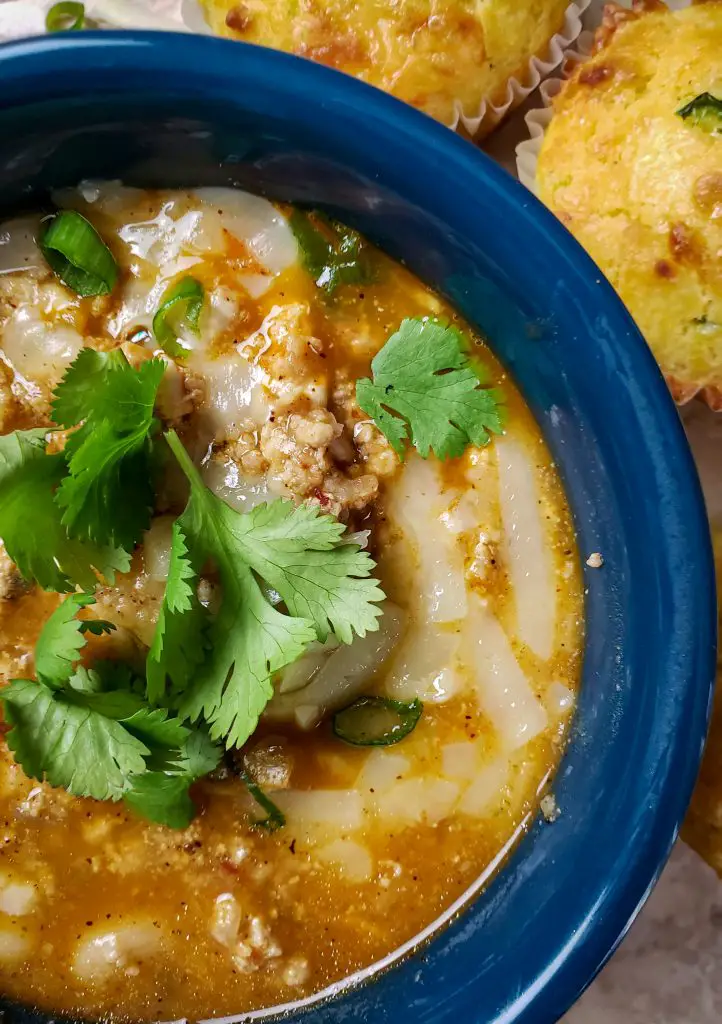 white bean turkey chili topped with cheese and cilantro in blue bowl served with cornbread