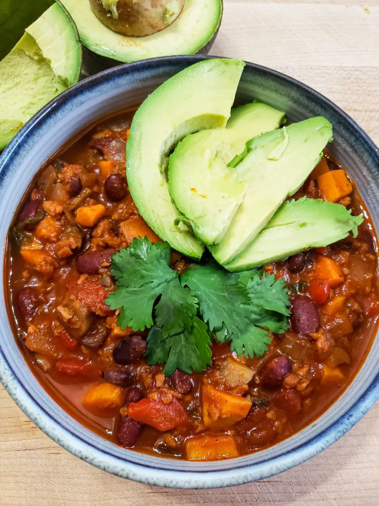 bowl of vegan chili with avocado slices and cilantro