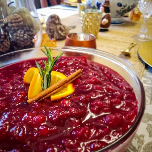 CRANBERRY SAUCE WITH APPLES AND ORANGE ZEST on thanksgiving table with orange peel , rosemary and cinnamon stick garnish