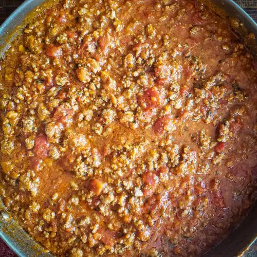 image of bolognese sauce in stainless steel pan sitting on dishtowel on table