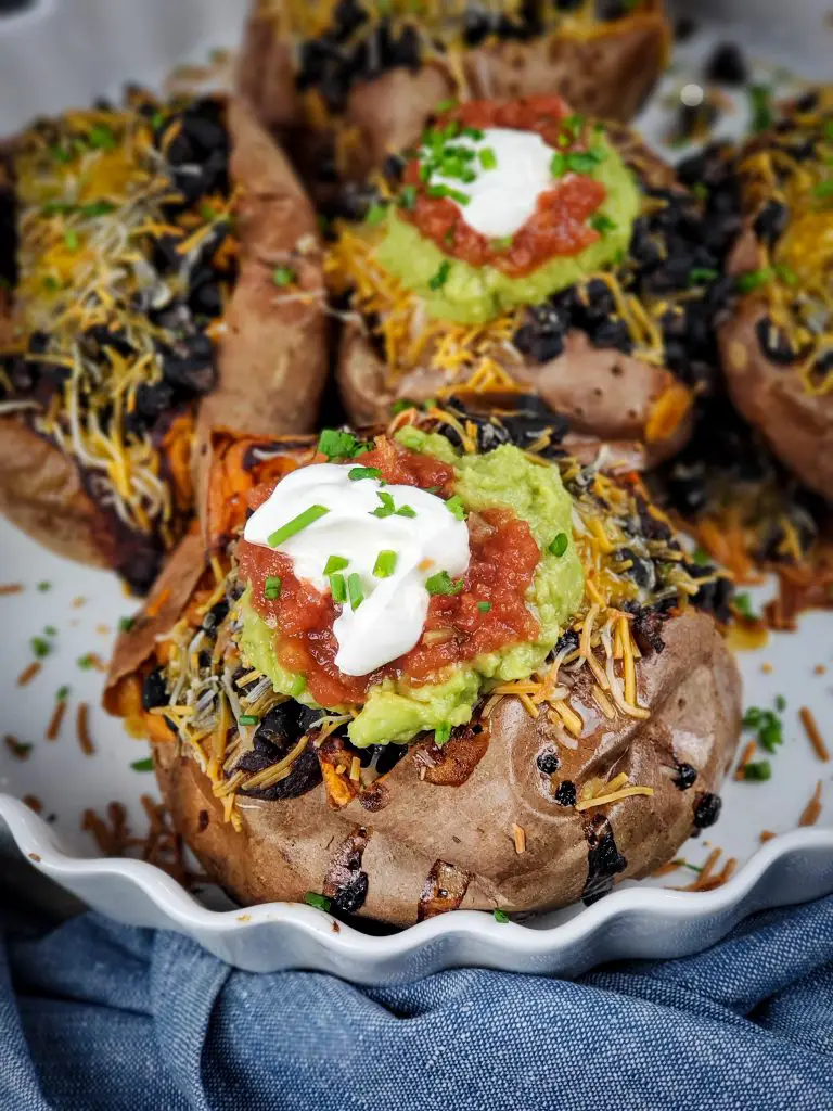 image of baking dish of black bean enchilada stuffed sweet potatoes topped with guacamole salsa and sour cream