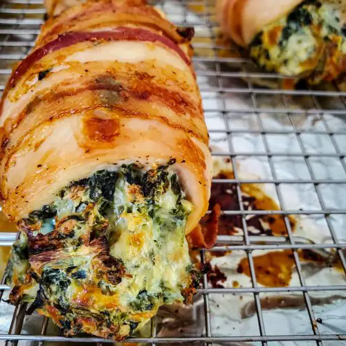 up close image of bacon wrapped spinach and artichoke stuffed chicken breast on wire baking rack