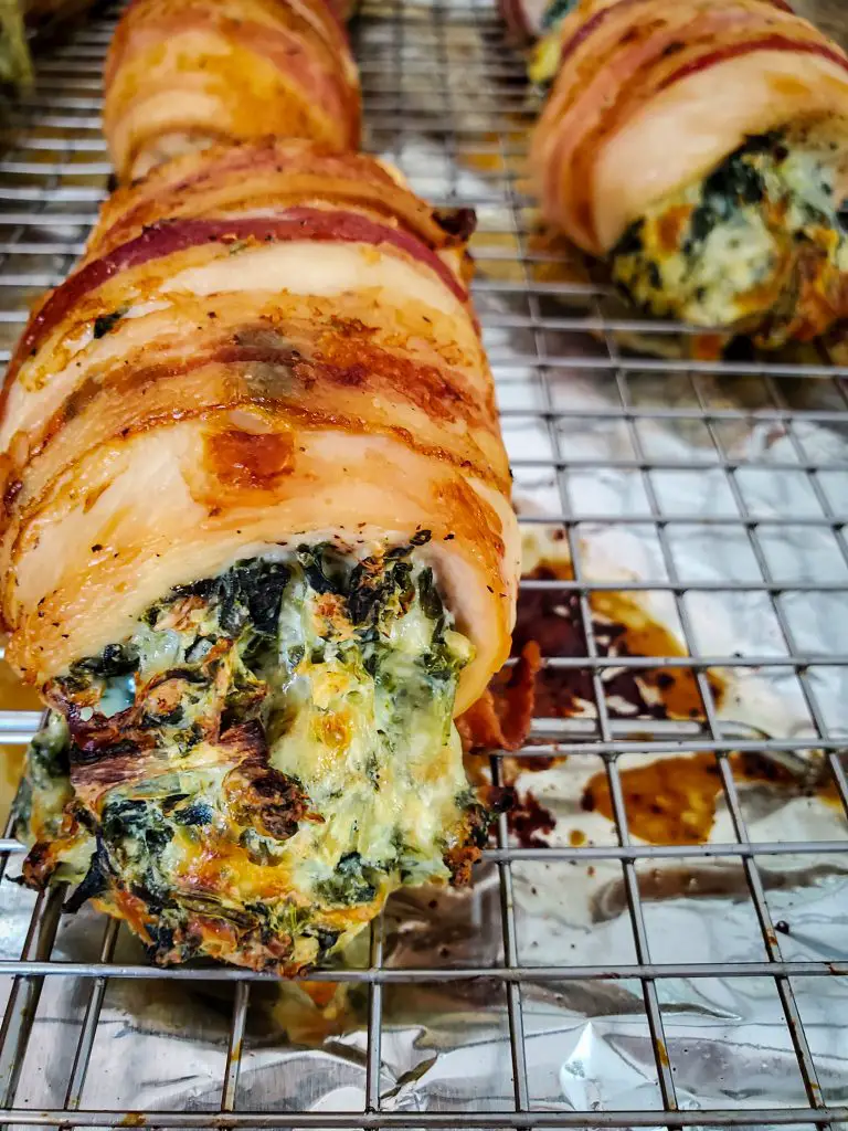 up close image of bacon wrapped spinach and artichoke stuffed chicken breast on wire baking rack