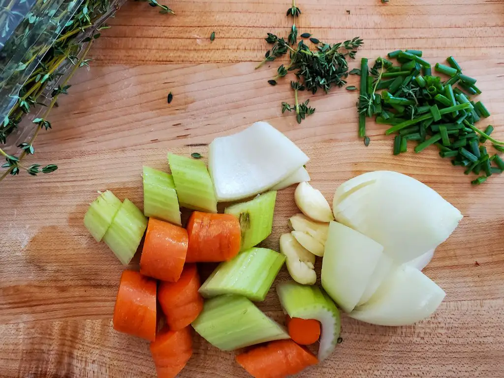 Bild von Sellerie, Karotte, Zwiebel, Knoblauch, Schnittlauch und Thymian auf dem Schneidebrett