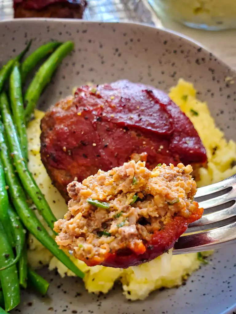 Bild einer Gabel, die einen Bissen Mini-Hackbraten mit Tomatenglasur hält, serviert mit Kartoffelpüree und grünen Bohnen