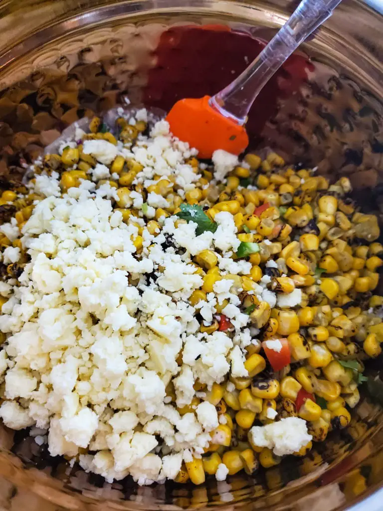 mexican street corn salad in mixing bowl with crumbled cojita cheese on top