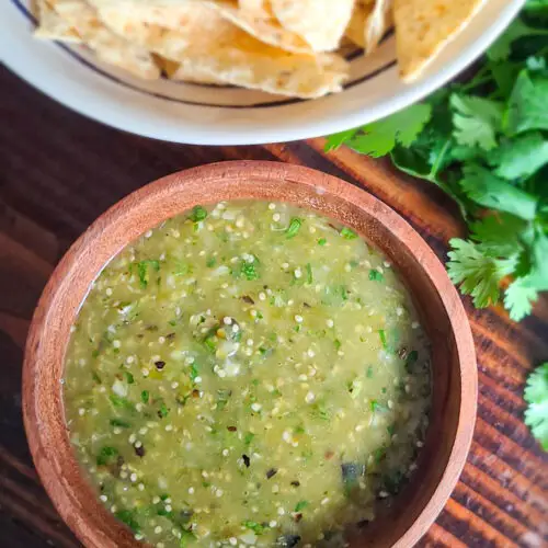 tomatillo salsa verde in small wooden bowl next to tortilla chips and sprig of cilantro