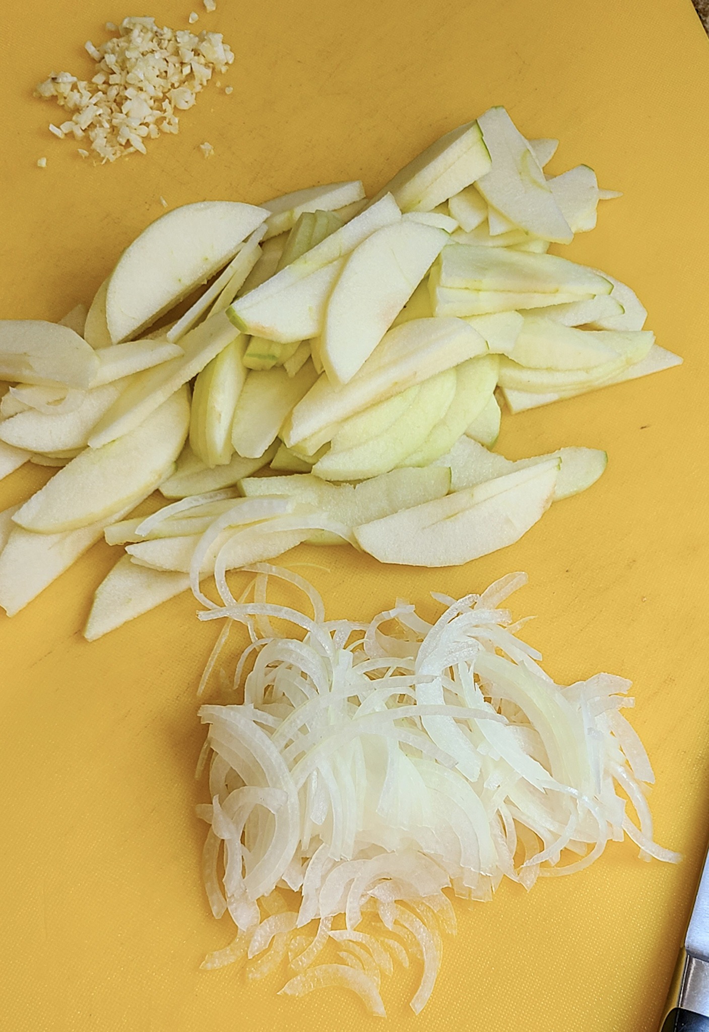 sliced apples, onions and garlic on yellow cutting board