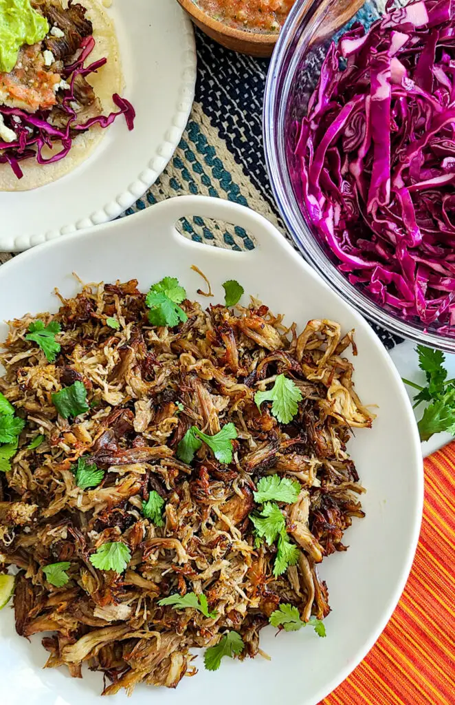 pork carintas in white serving platter on colorful table with red cabbage slaw and salsa