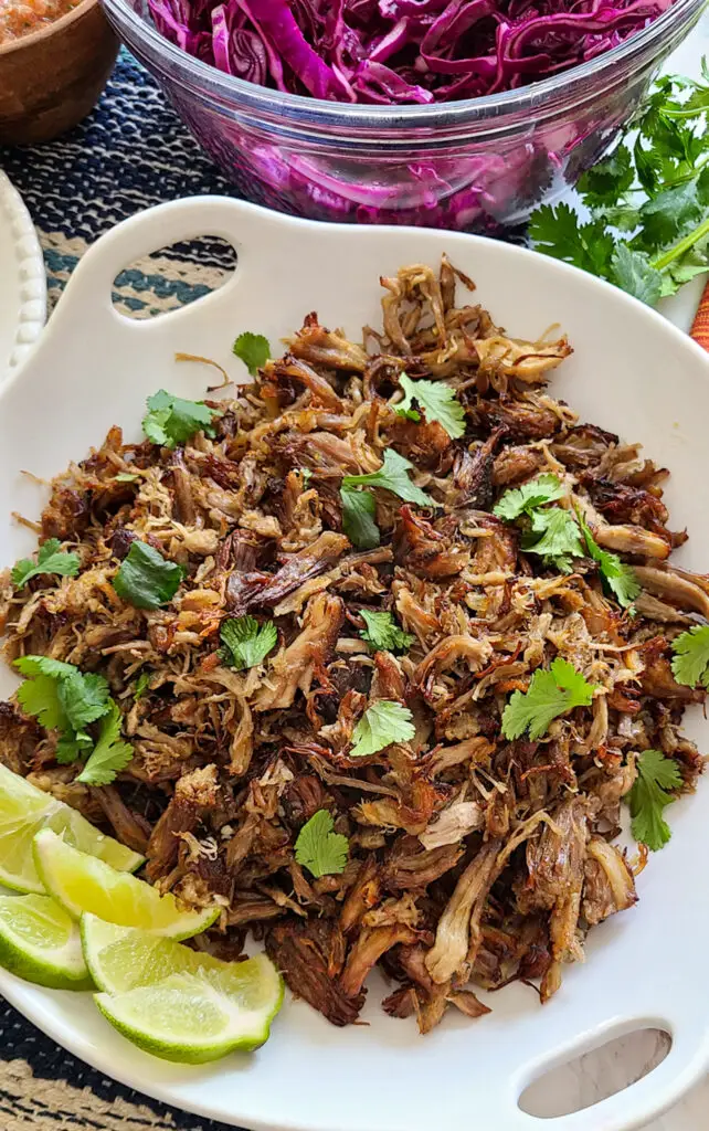 pork carnitas in serving platter with garnished with lime and cilantro