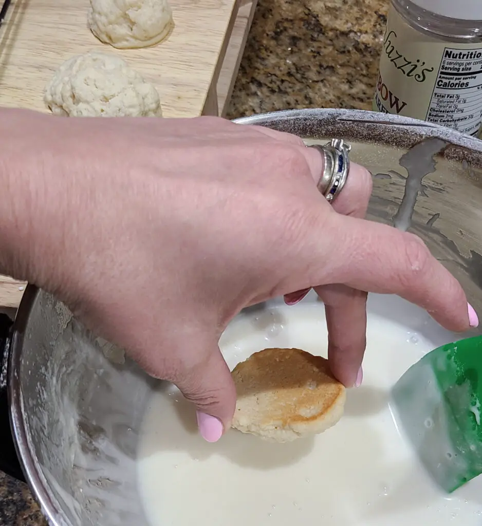 image of hand dipping a baked italian lemon ricotta cookie into a mixing bowl of vanilla icing
