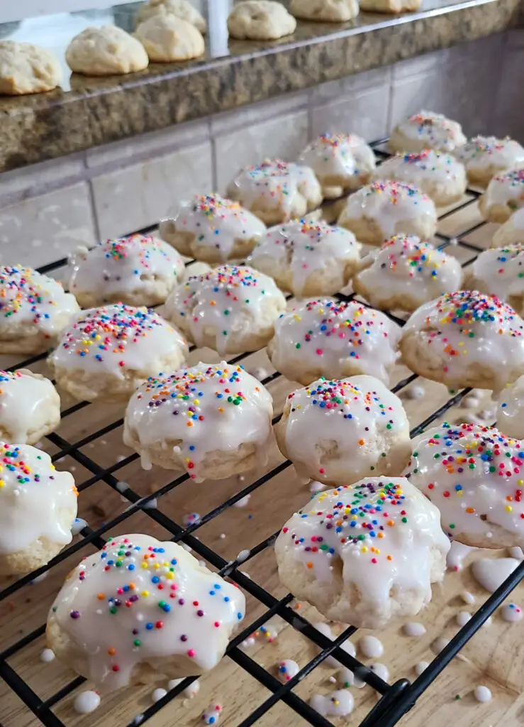 side view image of Italian lemon ricotta cookies with icing a sprinkles set on a cooling rack to dry