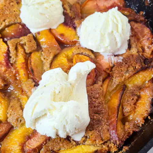 baked peach cobbler with vanilla ice cream in cast iron skillet
