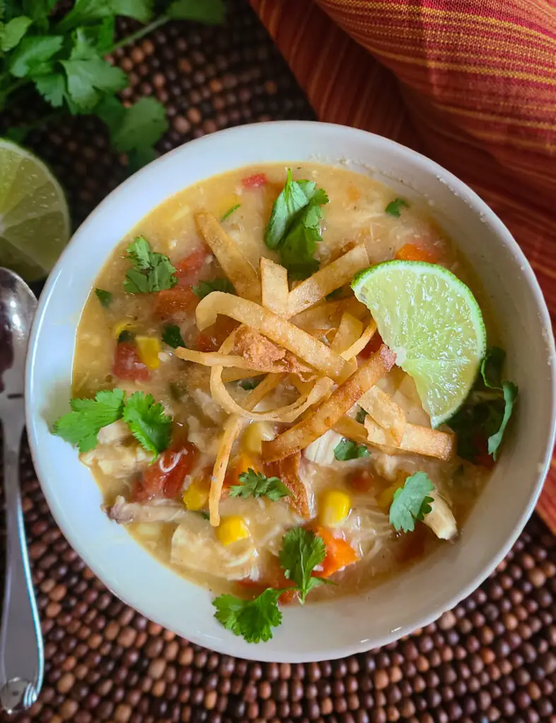 overhead image of bowl of chicken tortilla soup with crispy fried tortilla strips, lime wedge and cilantro as garnish